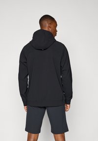 Black hooded sweatshirt with a smooth texture and fitted design. Features a kangaroo pocket and ribbed hem. Worn with matching shorts.