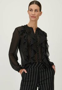Zwarte, doorzichtige blouse met witte stippen, met een gerimpelde voorkant en een collelloze ontwerp. Lange mouwen met knoopsluiting, gecombineerd met gestreepte broek.