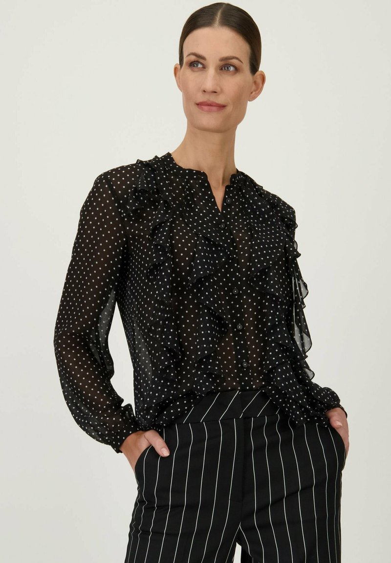 Zwarte, doorzichtige blouse met witte stippen, met een gerimpelde voorkant en een collelloze ontwerp. Lange mouwen met knoopsluiting, gecombineerd met gestreepte broek.