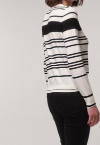 Pletený svetr v bílo-černých pruzích s kulatým výstřihem, dlouhými rukávy a žebrovaným lemem, v kombinaci s černými přiléhavými kalhotami.