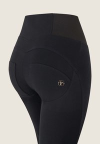 Leggings neri a vita alta realizzati in tessuto elasticizzato, con una texture liscia, cuciture curve e un piccolo logo dorato sull'anca.