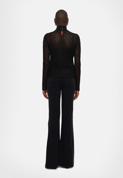 Schwarzes Langarmshirt aus transparenter Stoff mit zarten Blumenmustern, hoher Ausschnitt und einem kleinen Knopfverschluss im Rücken.