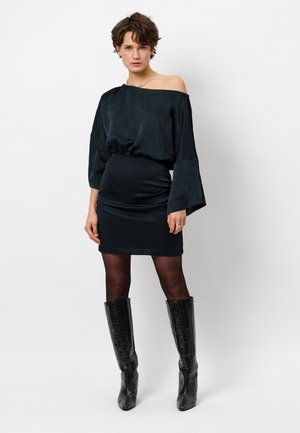 Zwarte off-shoulder jurk met klokmouwen en een aansluitende rok. G gedragen met glanzende zwarte kniehoge laarzen met krokodillenprint en sheer panty.