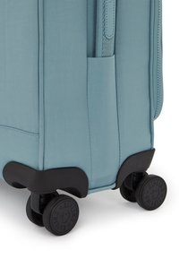 Light blue suitcase with a durable fabric exterior, side pocket, and four black swivel wheels for easy mobility.