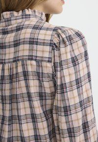 Ruudulise flanellist särk, millel on heledat roosa põhivärv ja tumedast hallist, meresinisest ning tanist triibud. Voogav krae ja puffi varrukad lisavad tekstuuri.