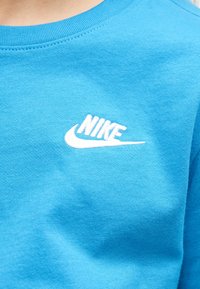 Κοντινή λήψη μπλε υφάσματος με λευκό λογότυπο Nike κεντημένο στην περιοχή του στήθους ενός ρούχου.