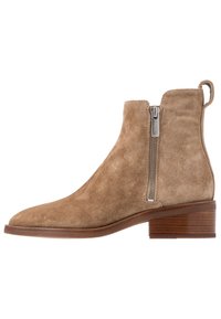 Beżowy zamszowy botek za kostkę z zaokrąglonym czubkiem, bocznym zamkiem błyskawicznym i niskim, warstwowym obcasem. Charakteryzuje się gładką fakturą i minimalnym przeszyciem.
