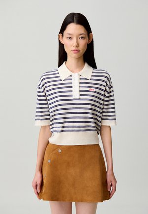 Polo de manga corta a rayas en crema y azul marino, con tapeta de botones y logo bordado; combinado con una minifalda de ante marrón con broches.