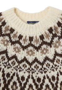 Pull en tricot base crème avec un motif géométrique marron. Design à col rond avec des coutures texturées et une étiquette visible au niveau du col.