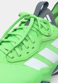 Neon green athletic shoe with textured mesh and smooth overlays. Features white stripes, a gray tongue, and intricate lace detailing.