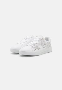 Zapatillas blancas con bordado floral en beige en los laterales exteriores. Incluyen un diseño de caña baja, punta redonda y cierre con cordones.