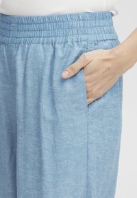 Svetlo modri, tkanih hlač z elastičnim pasom in stranskimi žepi; tkanina ima mehak, teksturiran finiš. Primerno za sproščeno nošenje.