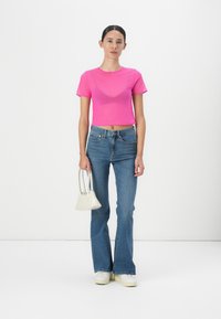 T-shirt corta di un vivace rosa, stile aderente; abbinata a jeans blu svasati e una piccola borsa bianca. Colori solidi, texture liscia, design semplice.