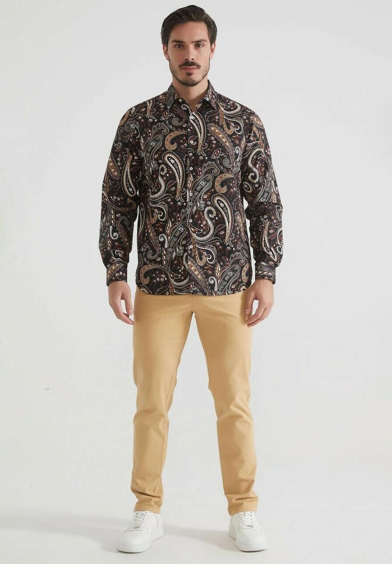 Chemise à manches longues en paisley dans des tons sombres avec des motifs complexes, associée à un pantalon beige et des baskets blanches. Tissu doux, coupe régulière.