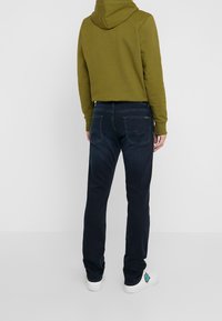 Olivgrön croppad hoodie med huva, i kombination med mörk denimjeans som har bakfickor och en lätt stretch. Vita sneakers med en accent.