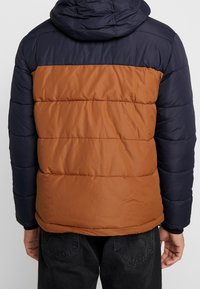 Kurtka puchowa z granatową górą i brązowym dołem, z pikowanymi sekcjami, kapturem i elastycznymi mankietami. Wykonana z gładkiego, lekkiego materiału.