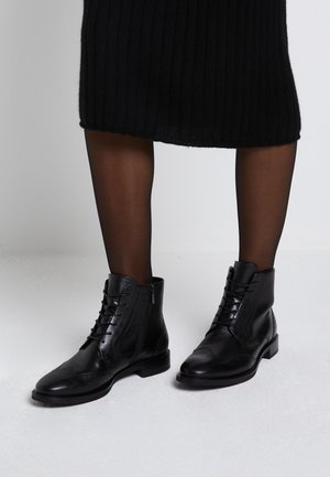 Bottines noires en cuir à lacets portées avec des collants noirs transparents et une jupe noire en maille côtelée.