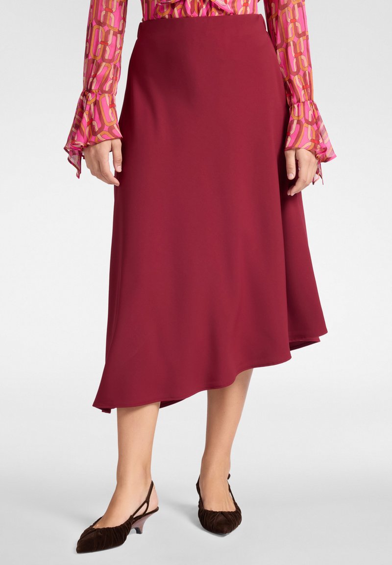 Falda A-line burdeos hecha de tela suave, con un dobladillo asimétrico. Combinada con zapatos slingback marrones de textura.