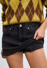 Shorts en denim noir à taille haute, avec poches avant, fermeture à bouton et ourlet légèrement effiloché. Tissu texturé visible.