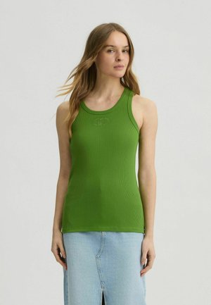 Grünes, geripptes Tanktop mit rundem Ausschnitt und Logodetail auf der Brust. Kombiniert mit einem hellblauen Jeansrock mit einem Schlitz vorne.