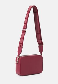 Červená kožená crossbody kabelka s obdélníkovým tvarem, texturovaným povrchem a vzorovaným látkovým popruhem. Obsahuje zlatý zip na uzavření.