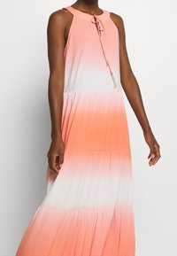 Maxi vestido con cuello halter, que presenta un degradado de coral a blanco, diseño en capas y un cordón con un acento de borlas.