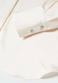 Gros plan sur le poignet d'une chemise blanche à manches longues avec deux petits boutons ronds sur un tissu lisse.