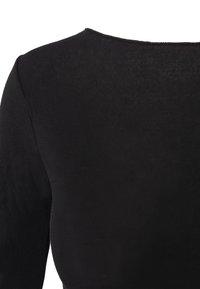 Maglietta nera a maniche lunghe con costine, caratterizzata da un collo rotondo e un tessuto testurizzato. La parte posteriore mette in risalto una finitura liscia con un sottile dettaglio di cucitura.