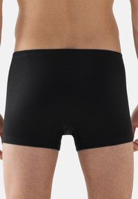 Vue arrière d'une personne portant un boxer ajusté noir uni avec une taille lisse et une longueur de jambe courte.