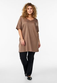Túnica marrón de manga corta con escote en V y corte holgado, combinada con pantalones negros. La tela es suave y tiene un ligero brillo.
