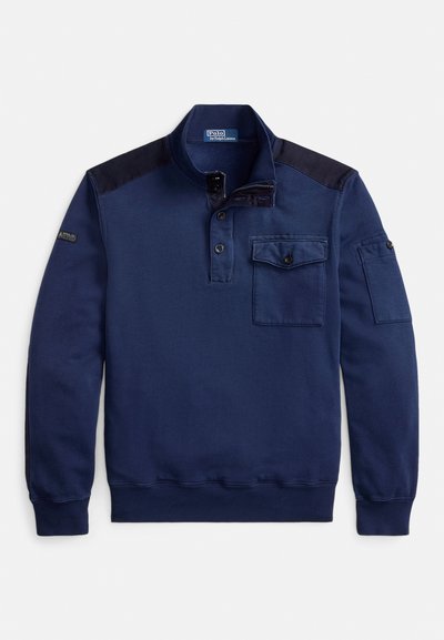 Mornarsko modra pulover jopica iz mehke tkanine, z odprtino s pol gumbov, žepom s preklopom in kontrastnimi črnimi ramenskimi paneli.