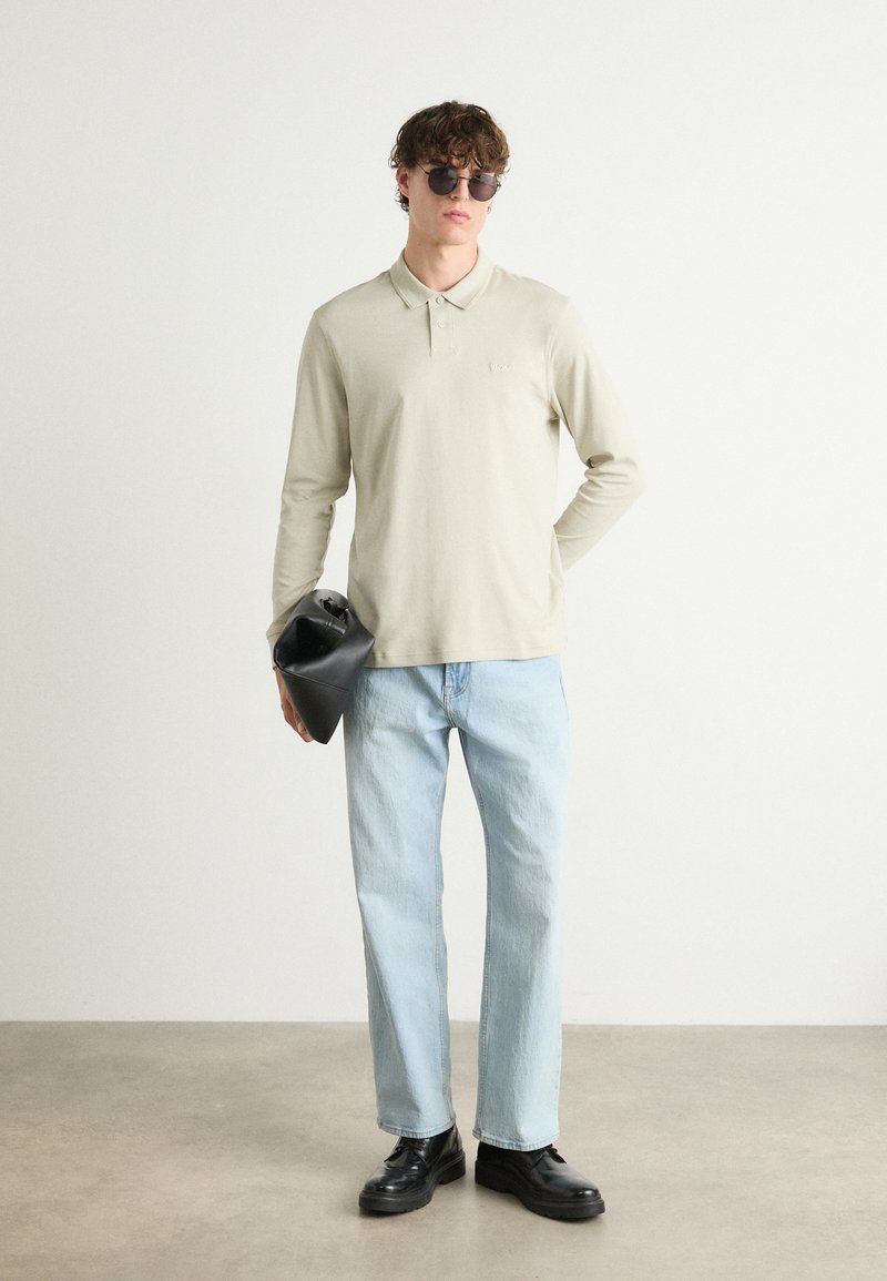 Polo-shirt beige clair à manches longues, jean bleu clair à coupe décontractée, bottes noires à semelles épaisses et sac fourre-tout noir.