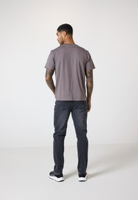Grå t-skjorte med korte ermer, sammen med mørke jeans. T-skjorten har en avslappet passform og glatt tekstur, sett fra baksiden.