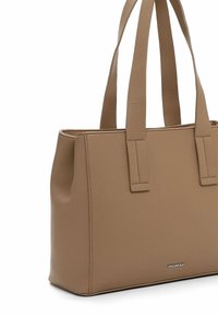 Brun læder tote bag med en struktureret form, dobbelte hænder og et subtilt prægede brandlogo på forsiden. Glat tekstur.