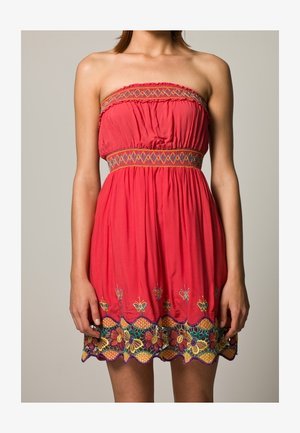 Korallivärinen olkaimeton mekko, jossa on joustava vyötärö. Mekossa on eloisaa kirjottua kukkakuviota helman kohdalla ja moniväristä yksityiskohtaisuutta.