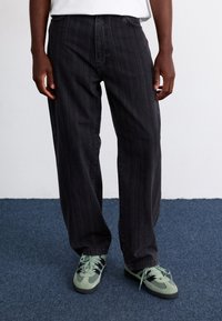 Schwarz gestreifte, locker sitzende Jeans mit hoher Taille, kombiniert mit hellgrünen Sportschuhen mit dunklen Akzenten und Schnürsenkeln.