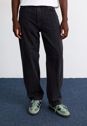 Jeans a vita alta a righe nere e larghe, abbinati a scarpe da ginnastica verde chiaro con accenti scuri e lacci.