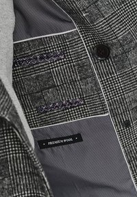 Wełniana kurtka z czarno-białym wzorem w szejk, z paskowanym podszewką i dekoracyjnym stębnowaniem kieszeni. Metka z napisem "PREMIUM WOOL."