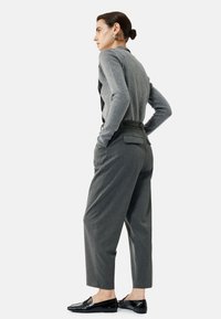 Pull en tricot gris avec motif en losange, pantalon gris taille haute avec ceinture, et mocassins noirs. Le mannequin porte un chignon lisse et des boucles d'oreilles.