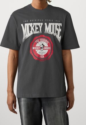 Osoba ubrana w ciemnoszarą koszulkę z vintage logo Myszki Miki oraz białym i czerwonym napisem „The Original since 1928” na przodzie.