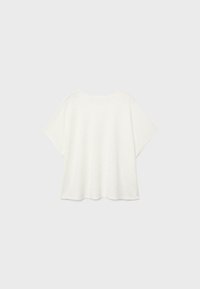 Chemise ample blanche à manches courtes avec un col rond, présentée sur un fond gris clair.