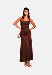 Braunes glitzerndes Maxikleid mit geradem Ausschnitt und Raffung, kombiniert mit metallischen Plateau-Schuhen mit Knöchelriemen und einer kleinen Clutch.