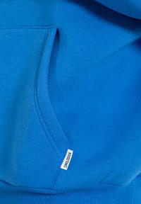 Blauwe sweatshirt met een voorzak, ribbelboorden, een gladde textuur en een klein wit etiket met "SMILODOX" aan de zijkant.