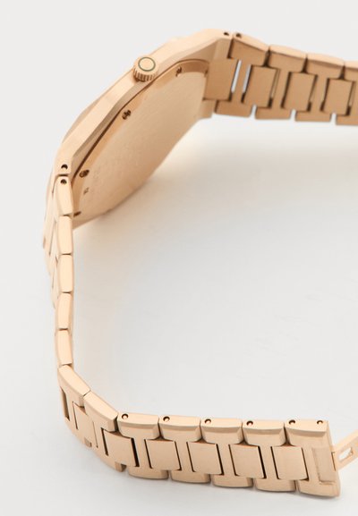 Ρολόι χειρός από ροζ χρυσό μέταλλο που δείχνει την πίσω θήκη και τον συνδεδεμένο βραχίονα σε λευκό φόντο.