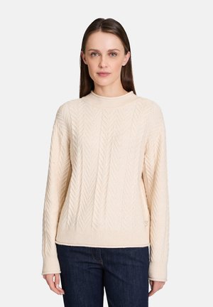 Krämfärgad kabelstickad tröja med hög krage, långa ärmar, ribbad fåll och strukturerad mönster. Kombination med mörka jeans.