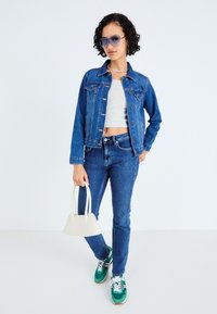 Kék farmerdzseki és farmernadrág, szürke crop top-pal, zöld és fehér sportcipővel, valamint egy kis fehér kézitáskával párosítva. Nagy kék napszemüveg.