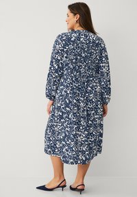 Robe midi florale marine à manches longues, taille smockée et imprimé botanique blanc. Assortie à des escarpins à talons marine.