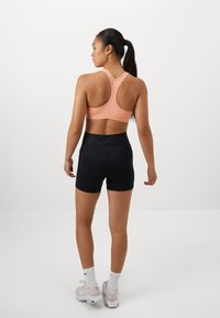 Reggiseno sportivo in pesca con design a dorso scoperto, abbinato a pantaloni corti neri. Tessuto liscio, silhouette aderente e dettaglio del logo a contrasto sull'elastico.