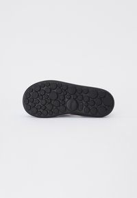 Black rubber shoe sole featuring a textured surface with circular patterns and a prominent brand logo. Smooth edges and curved shape.