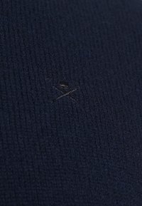 Granatowa, teksturowana tkanina z subtelnym, czarnym wyszywanym logo. Tło ma jednolity, prążkowany wzór.